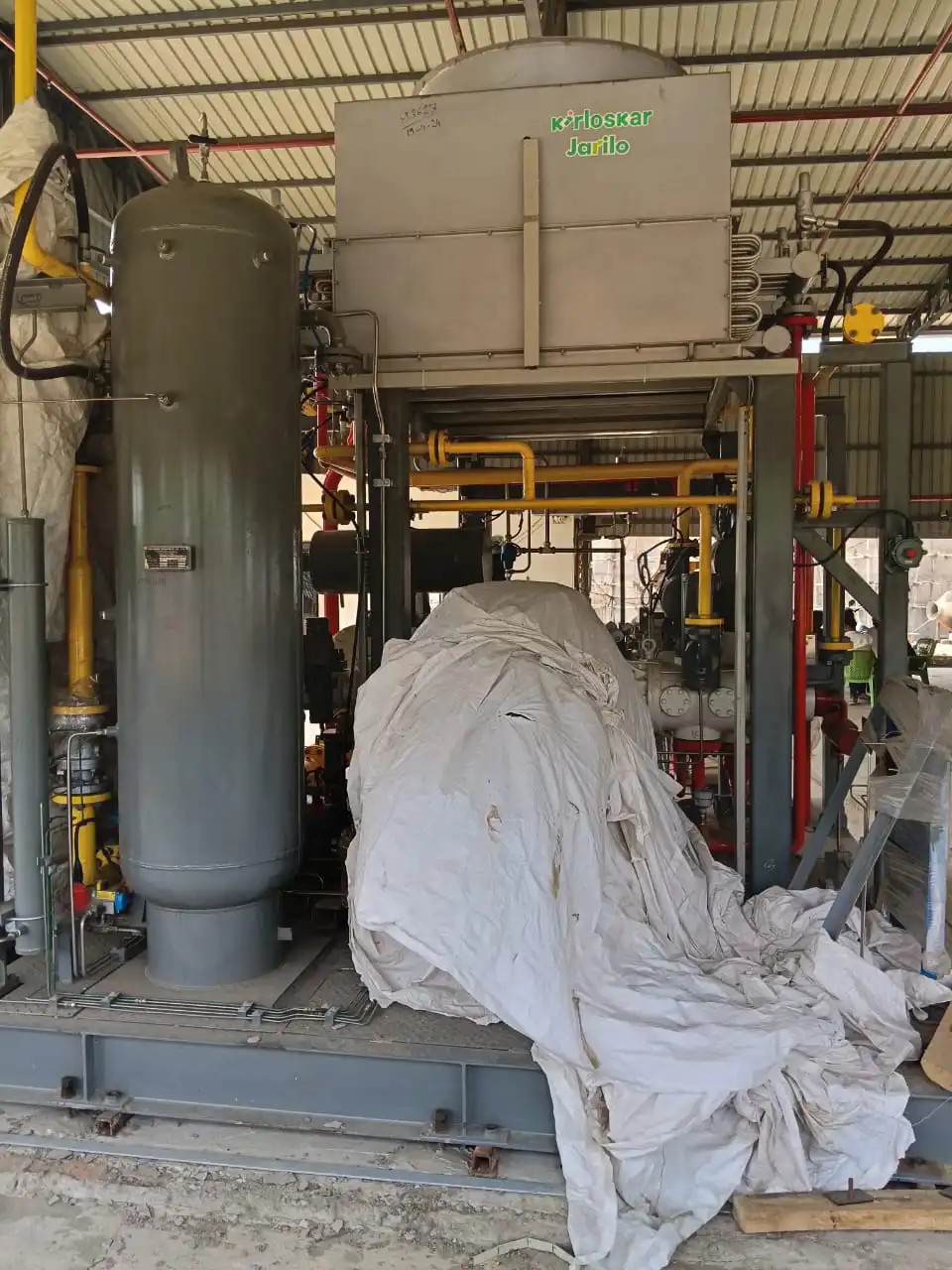 Gas compression skid with a grey pressure vessel, cooler and yellow gas piping under a shed roof
