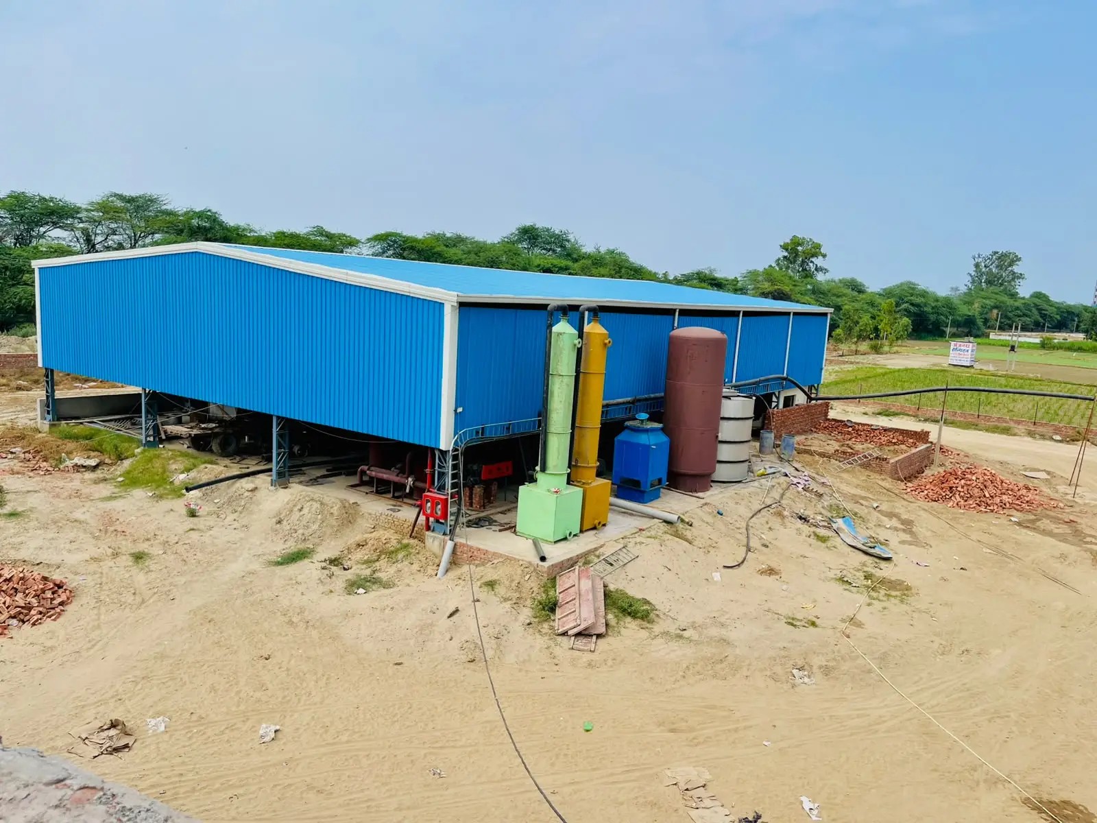 Blue steel processing shed with green and yellow scrubber columns and storage vessels beside it